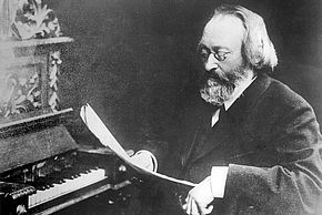 Photo en noir et blanc du compositeur Max Bruch en train de lire une partition devant un piano